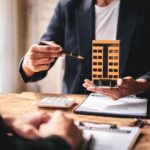 A man is holding a model of a building and pointing to it
