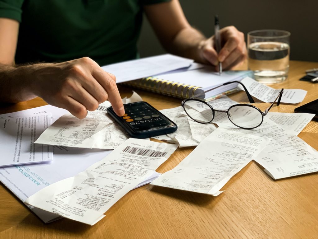 Man is making audit of household expenses using calculator and notebook. Lots of receipts and bills