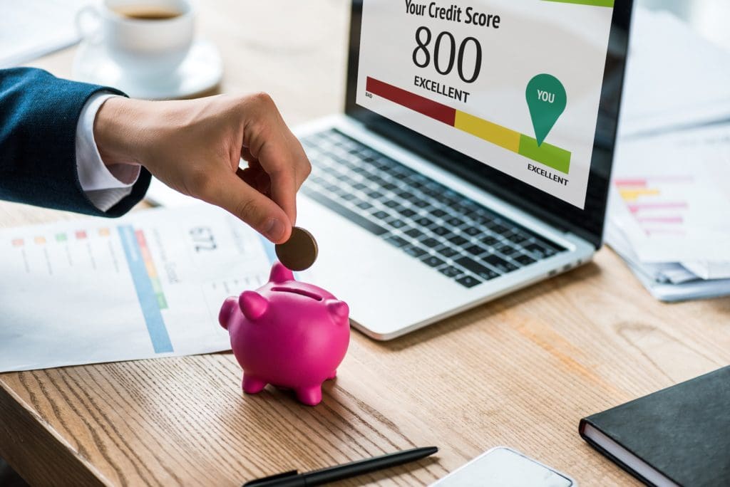 cropped view of businessman putting coin into pink piggy bank near laptop with your credit score