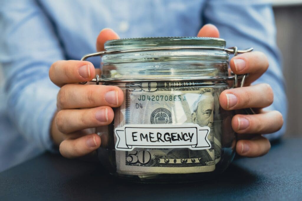 Female hands Saving Money In Glass Jar filled with Dollars banknotes. EMERGENCY transcription in